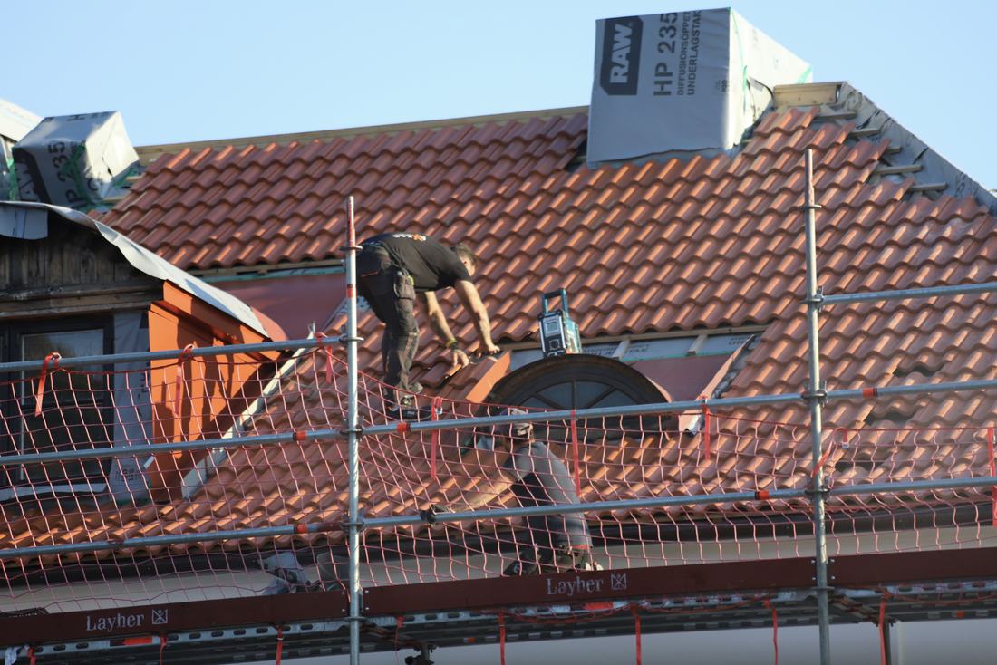 Roofer laying tiles on a pitched roof behind scaffolding